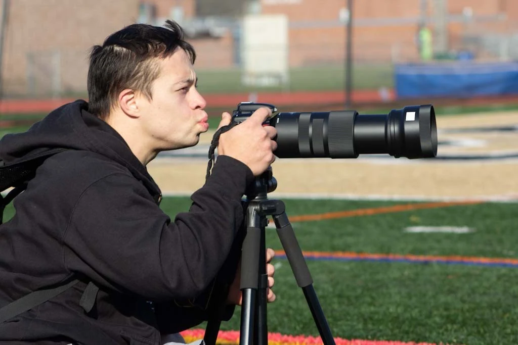 David looking through a telephoto camera on a sports field